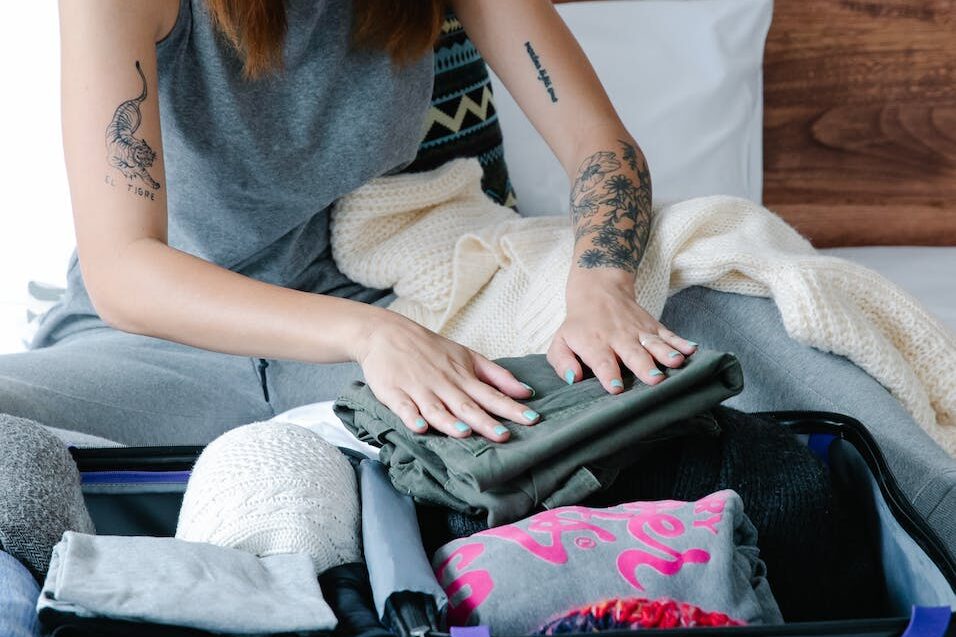 a woman in gray tank top folding clothes on a suitcase