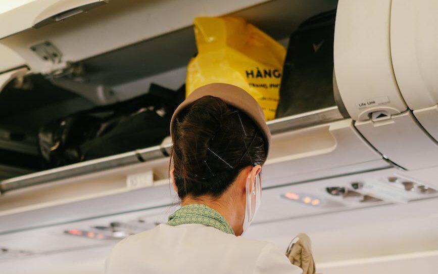 stewardess on plane cabin crew flight attendant overhead bin over head compartment