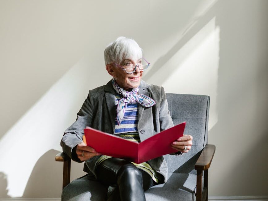 an elderly woman sitting on the chair holding a red folder while looking afar